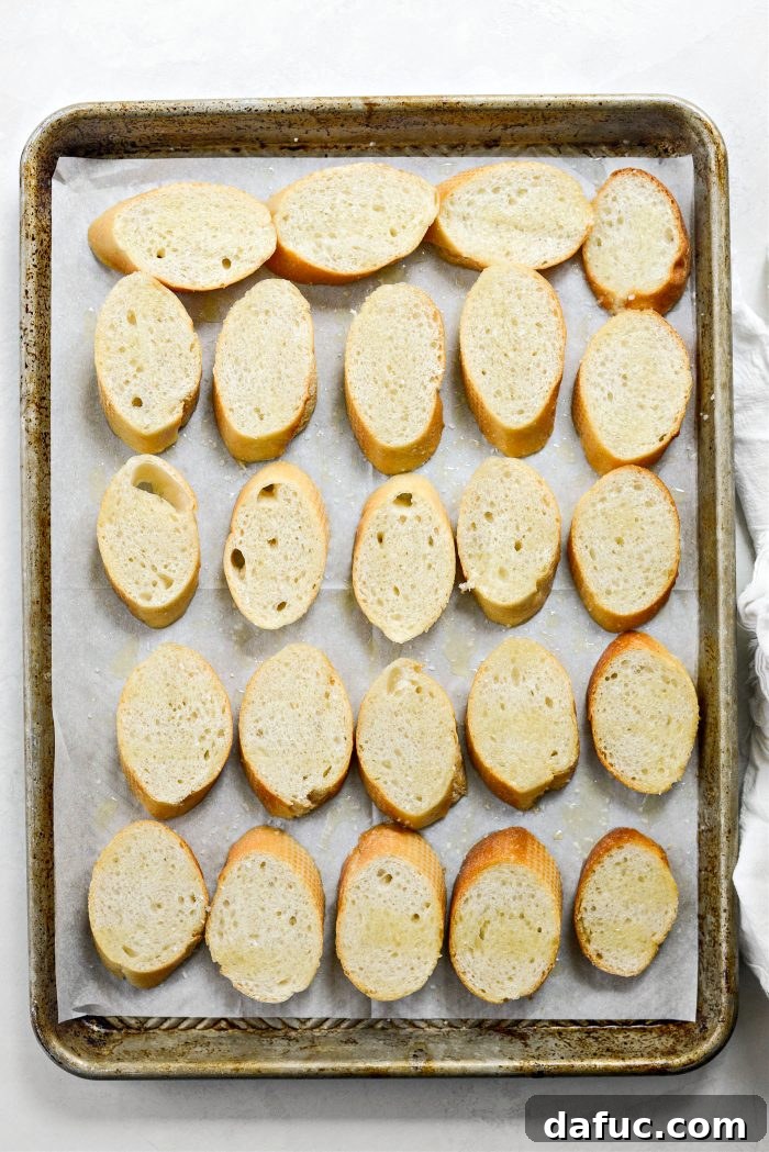 Sweet Blistered Tomatoes, Creamy Burrata, Crispy Pancetta 6 Sliced baguette pieces arranged on a rimmed baking sheet, ready for toasting.