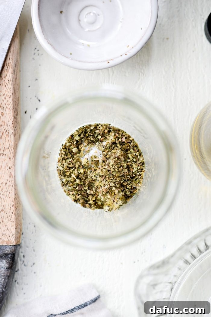 Adding crushed oregano to a jar with garlic, salt, and pepper