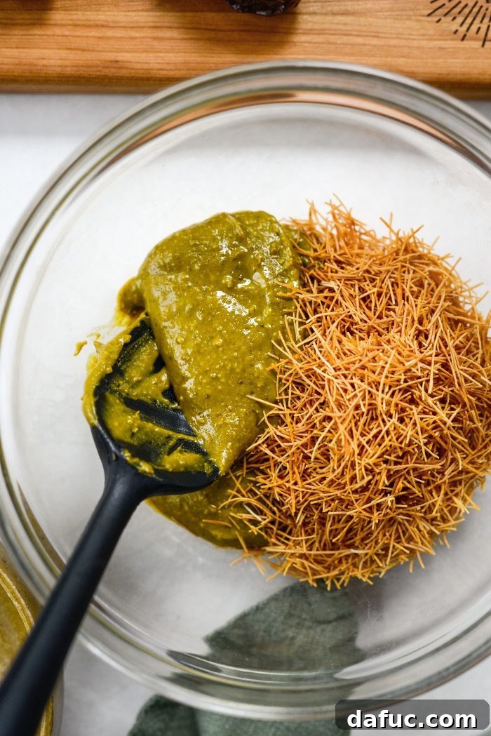 Pistachio cream and toasted kataifi being added to a mixing bowl
