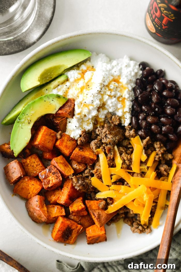 A vibrant Sweet Potato Beef Bowl with Hot Honey, showcasing roasted sweet potatoes, ground beef, cottage cheese, black beans, and avocado, all drizzled with hot honey.