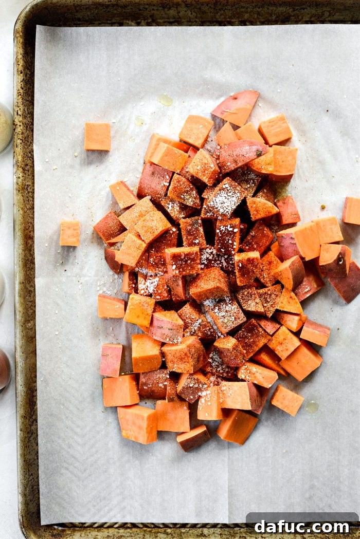 Diced sweet potatoes tossed with avocado oil and various spices on a baking sheet.