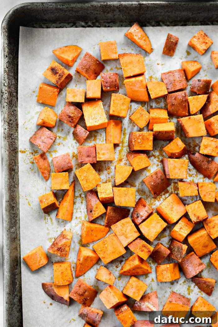 Diced sweet potatoes, oil, and spices being tossed on a baking sheet before roasting.