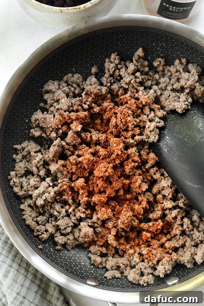 Cooked ground beef in a skillet with seasoning sprinkled over it.