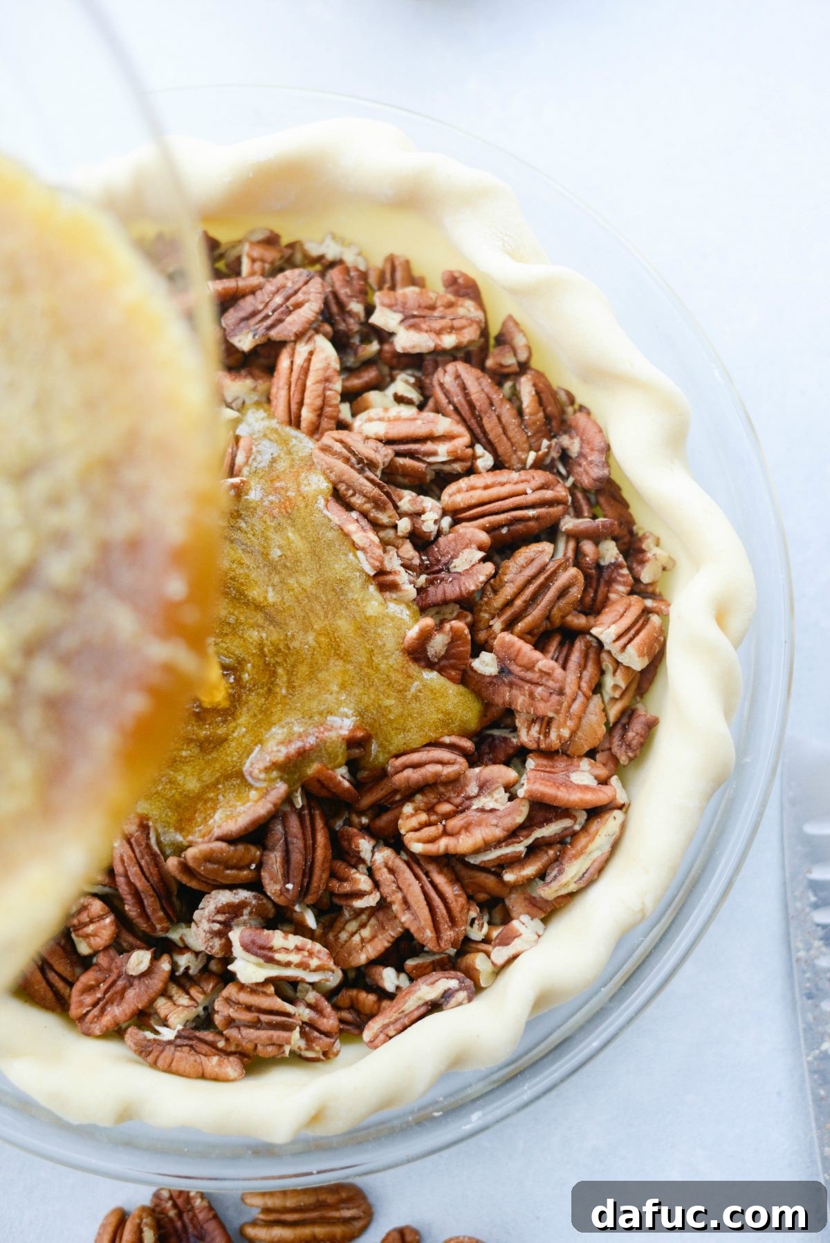 Irresistible Classic Pecan Pie 15 Pouring the filling over top of the pecans.