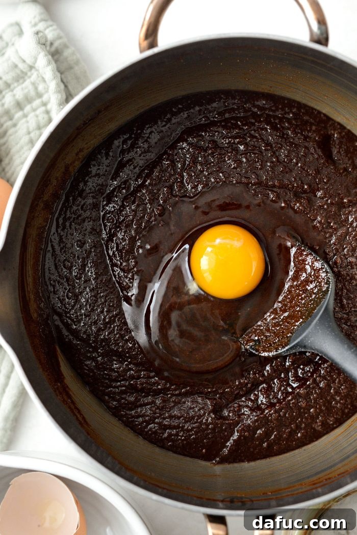 Adding one large egg at a time to the brownie mixture, whisking after each