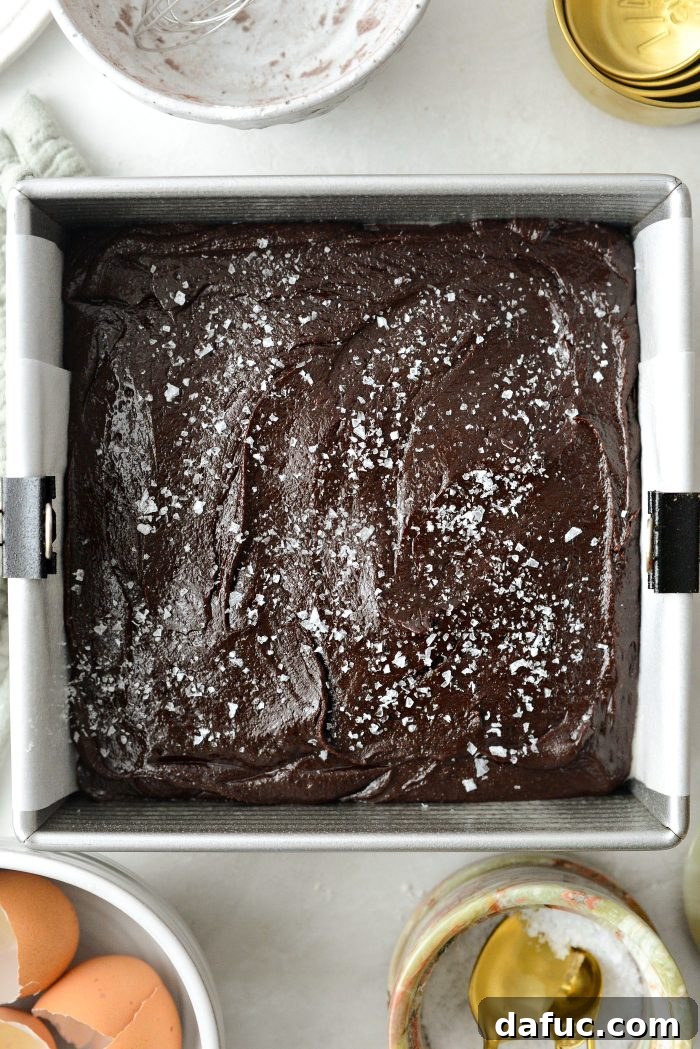 Pouring brownie batter into the prepared pan, spreading, and sprinkling with flaky salt