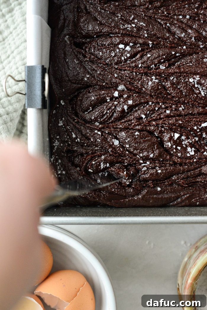Using a butter knife to gently swirl flaky sea salt into the brownie batter