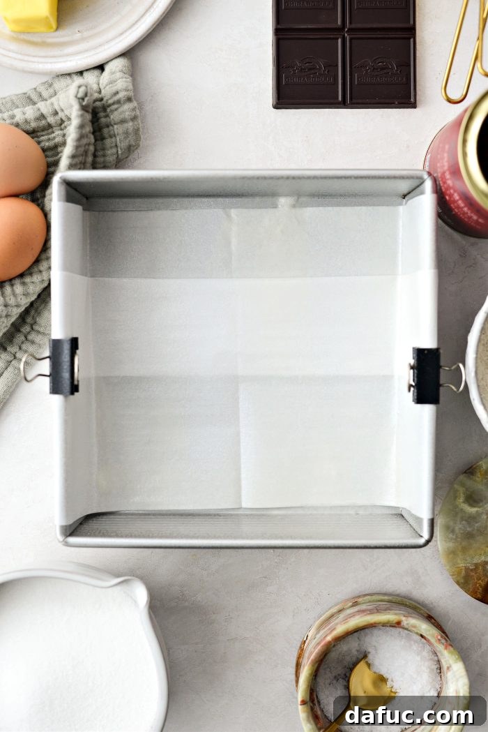 An 8x8 inch baking pan being lined with parchment paper, prepared for brownie batter