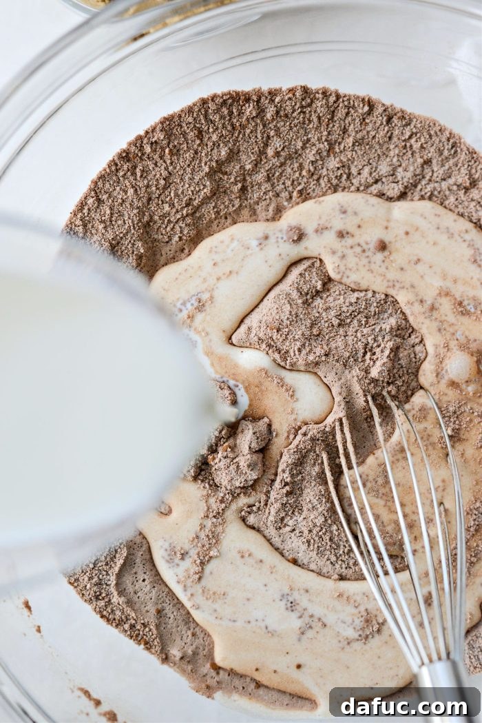 Milk being poured into the dry ingredients for Chocolate Pudding Cake in a mixing bowl