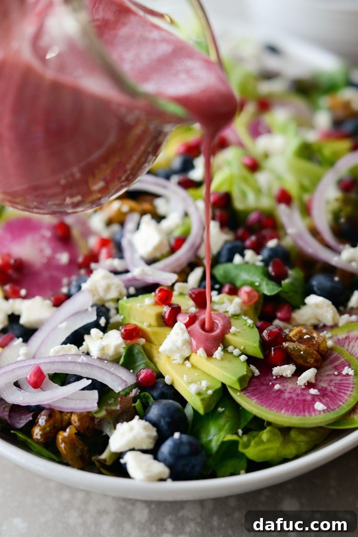 Pouring creamy pomegranate dressing over the fully assembled Blueberry Pistachio Spring Salad.