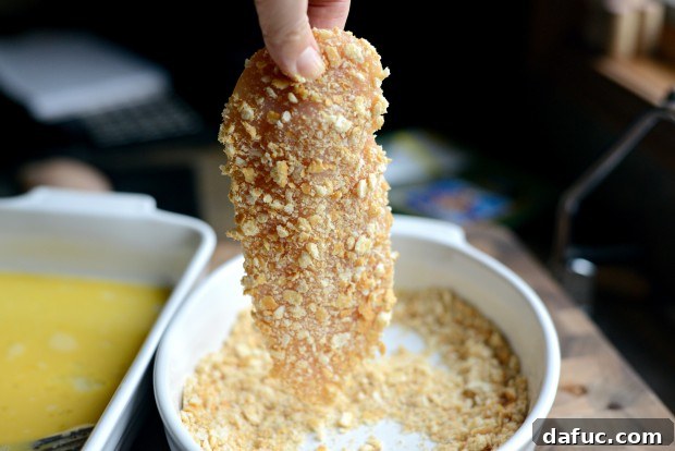 Pressing chicken into cracker crumbs for full coating