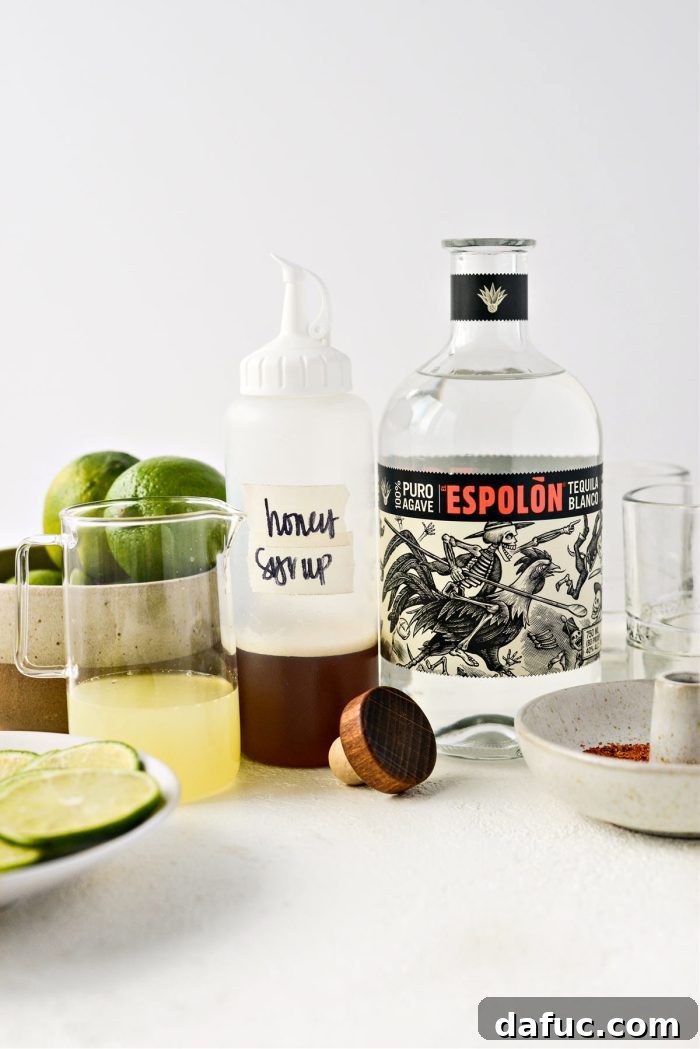Ingredients for Honey Lime Margaritas laid out: limes, a bottle of tequila, and a jar of honey.