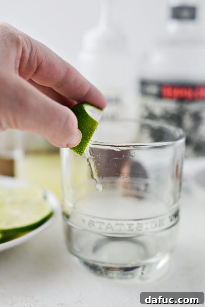 A hand rubbing the rim of a cocktail glass with a lime wedge.