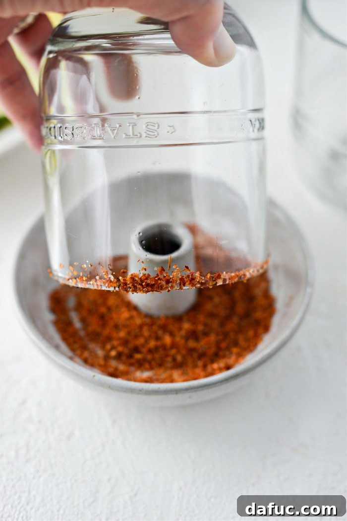 A cocktail glass being dipped into a plate of chili lime salt to coat the rim.