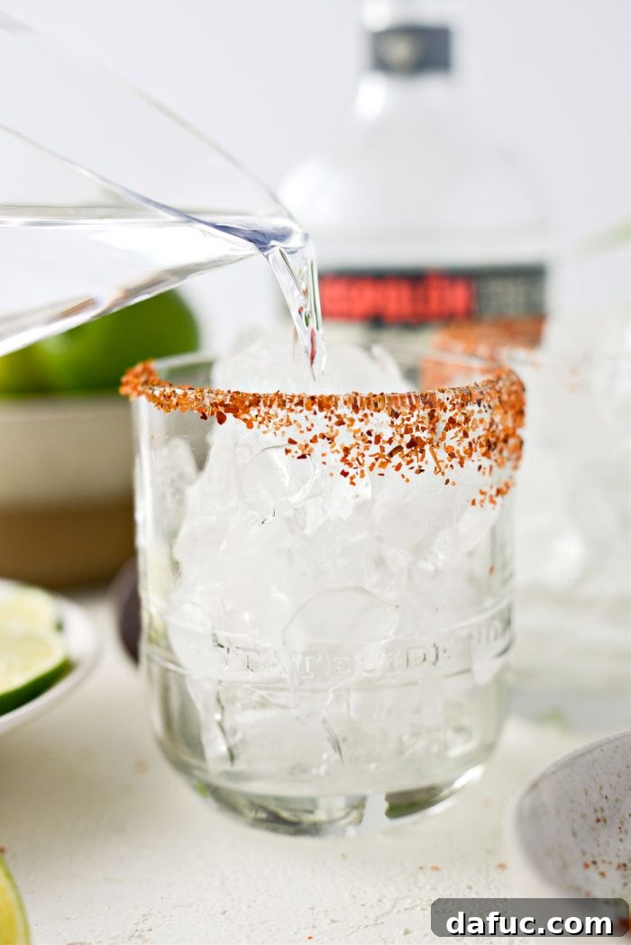 A hand pouring tequila over ice in a prepared cocktail glass.