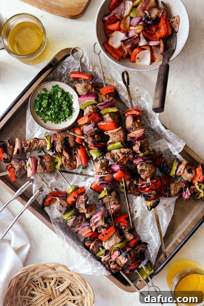 Platter of grilled marinated steak kebabs on a wooden tray with two glasses of beer