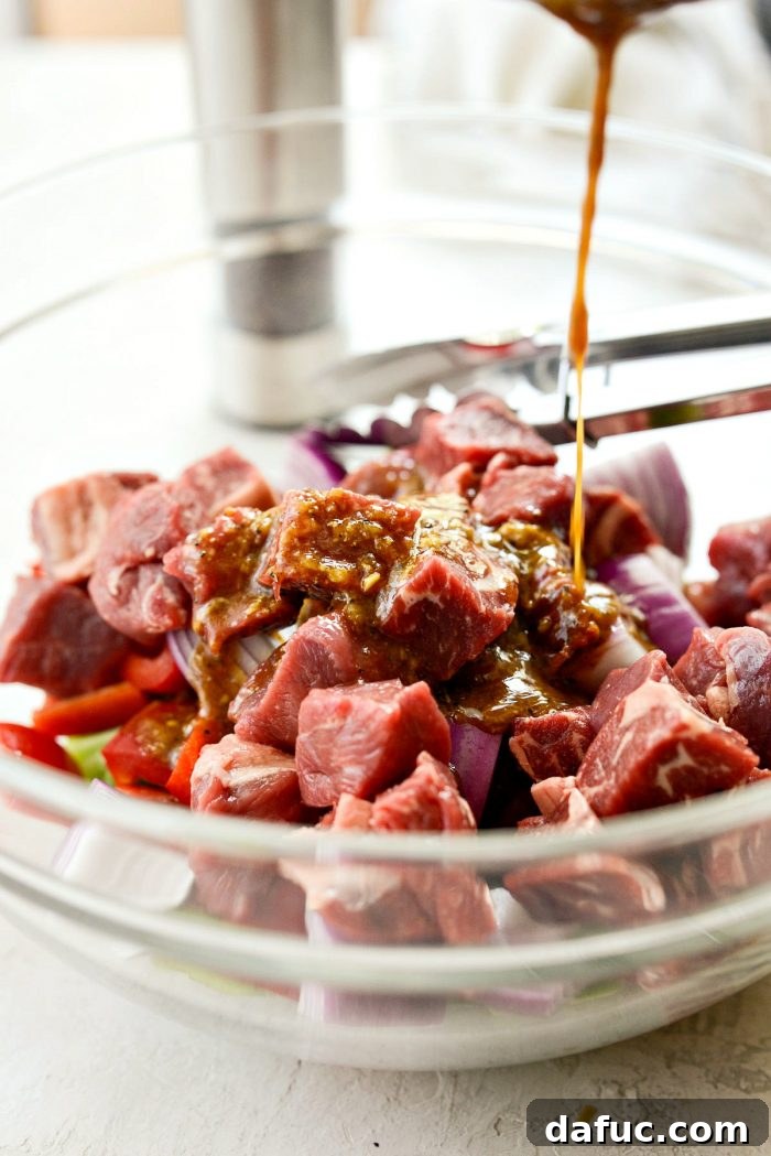 Cubed steak, bell peppers, and red onion mixed in a glass bowl, ready for marinade