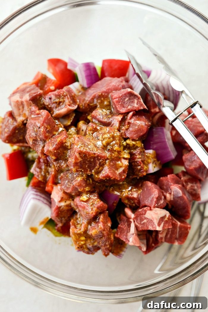 Top-down shot of steak, peppers, and onions coated in marinade in a glass bowl