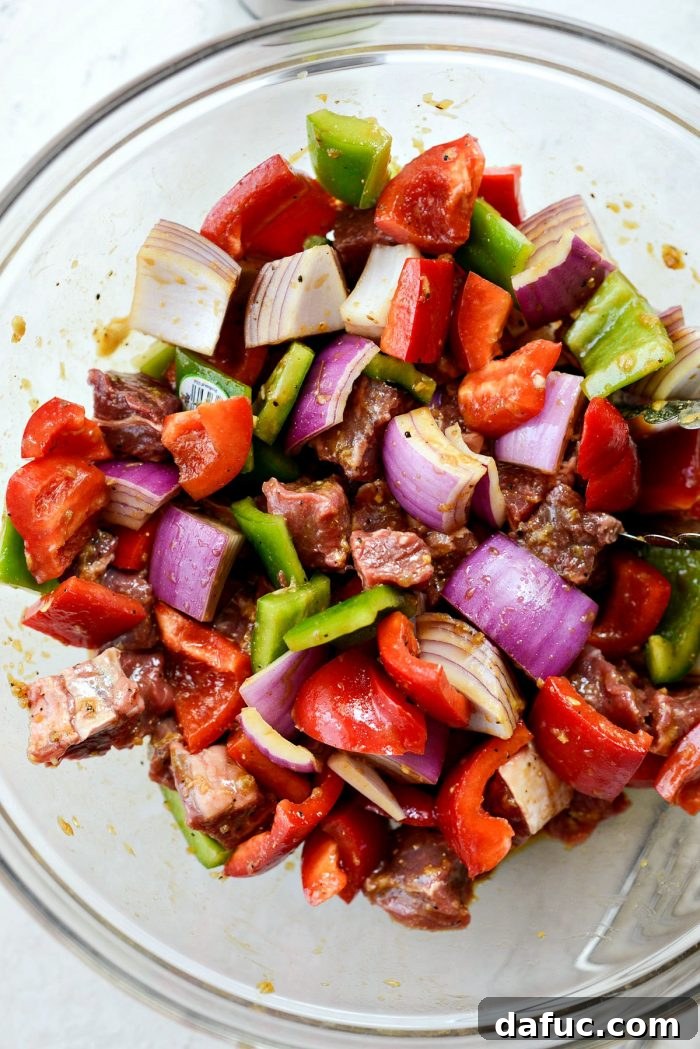 Steak and vegetables thoroughly tossed with marinade in a glass bowl