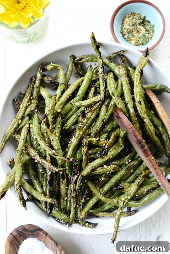 A bowl full of freshly grilled green beans, with tongs resting beside them, ready for serving.