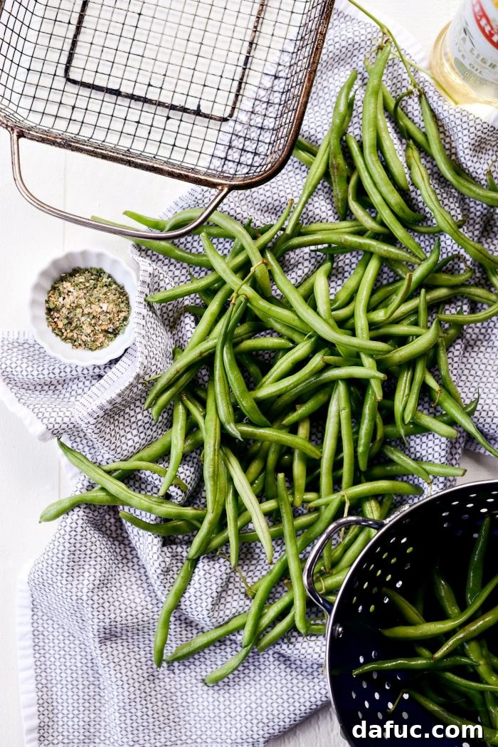 Ingredients for Grilled Green Beans laid out on a cutting board, including fresh green beans, olive oil, and a jar of garlic herb seasoning.