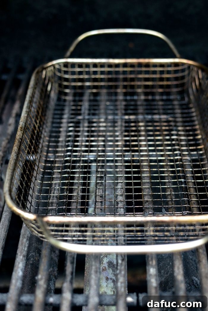 Preheating a grill basket on hot grill grates, ready for vegetables.