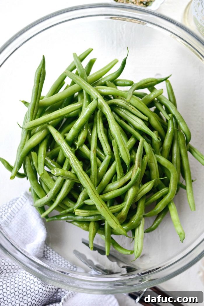 Cleaned and trimmed green beans in a clear glass bowl, ready for seasoning.
