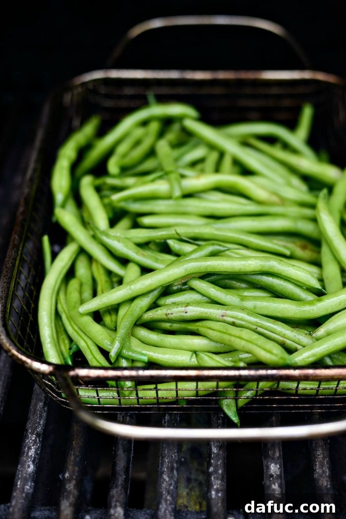 Green beans actively grilling inside a hot grill basket on a barbecue, showing early char marks.