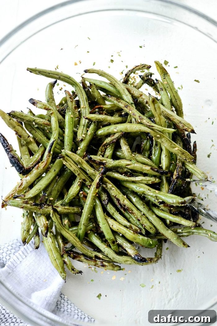 Grilled green beans tossed with garlic herb seasoning in a mixing bowl, showcasing even distribution.