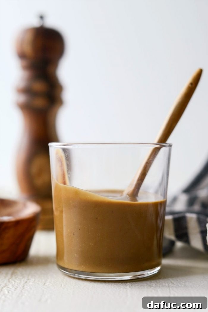 Signature Balsamic Vinaigrette 2 A beautiful glass jar filled with freshly made house balsamic vinaigrette, showcasing its rich golden-brown color and smooth, inviting texture on a wooden surface.