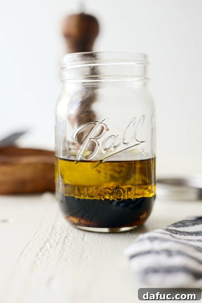 Signature Balsamic Vinaigrette 4 A clear glass mason jar containing the measured ingredients for balsamic vinaigrette, including olive oil, balsamic vinegar, Dijon mustard, honey, and minced garlic, ready for vigorous shaking.