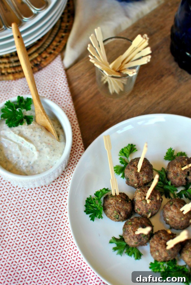 Close-up of baked mini gyro meatballs, garnished with fresh herbs, showcasing their golden-brown exterior.