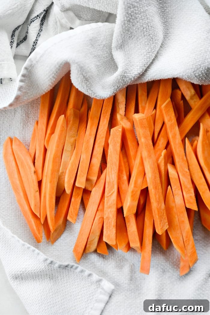 Sweet potato fries being dried thoroughly with a clean kitchen towel