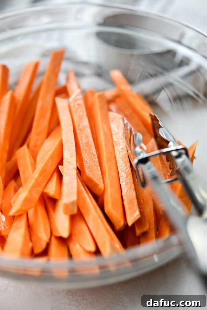 Sweet potato fries being tossed to evenly coat with avocado oil