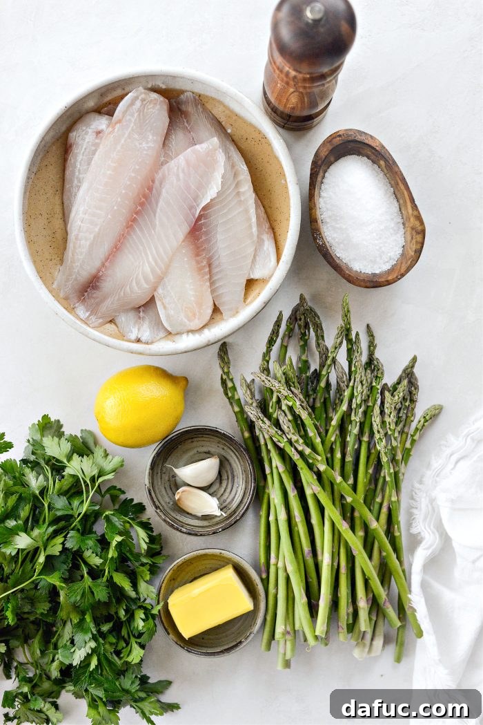 Fresh ingredients for Sheet Pan Lemon Garlic Tilapia with Asparagus laid out on a board