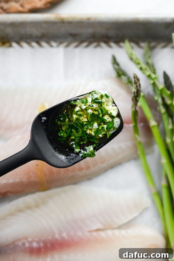 Spoon lemon garlic butter over fish and asparagus on a baking sheet