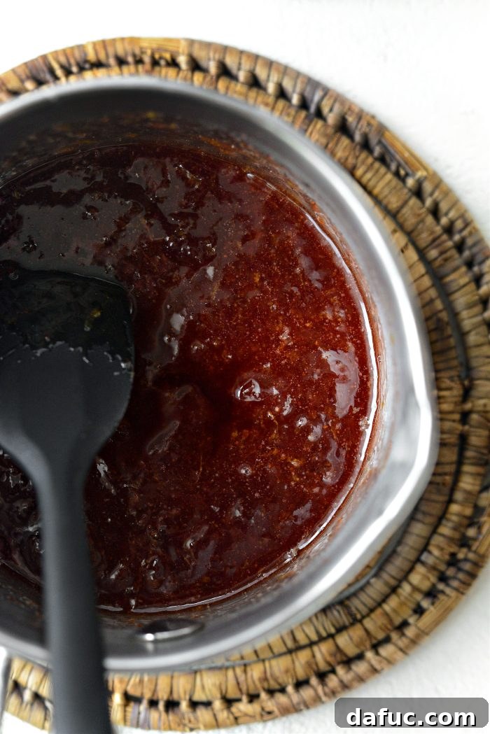 Heating strawberry jam and lemon zest in a saucepan, then adding vanilla extract