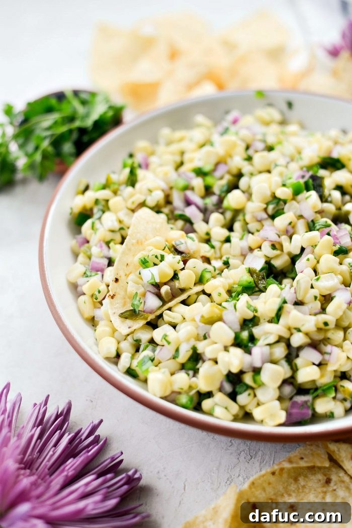 Chipotle's Signature Sweet Corn Salsa 3 A close-up view of homemade Chipotle Sweet Corn Salsa in a white bowl, highlighting the fresh and finely diced ingredients such as sweet corn, red onion, cilantro, and poblano pepper pieces. The bright colors suggest a refreshing and flavorful dish.