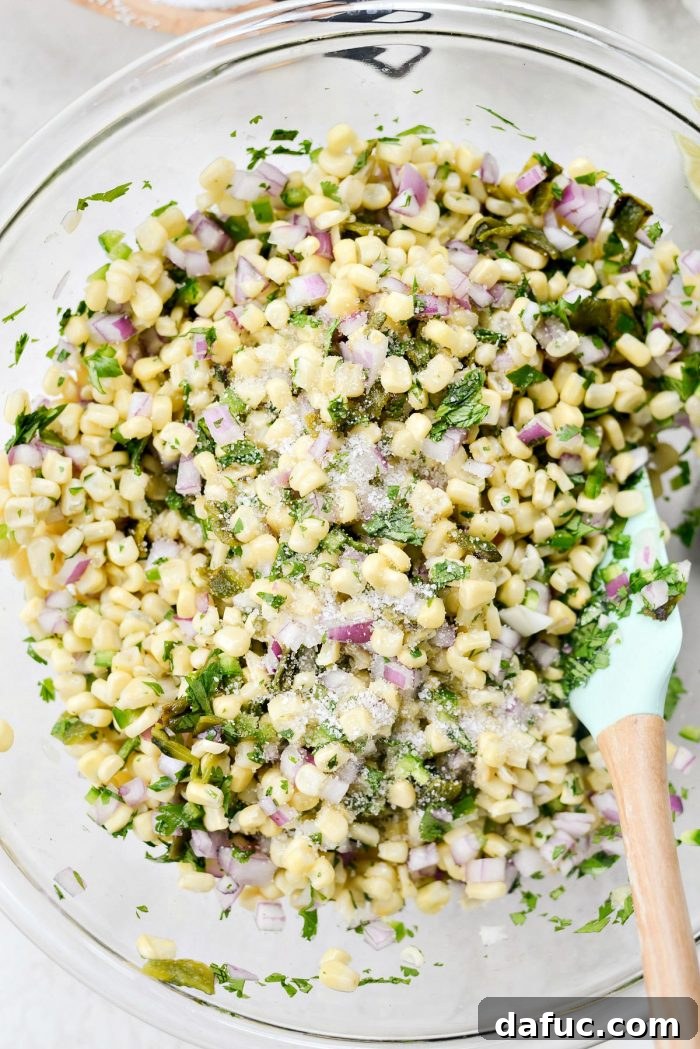 Chipotle's Signature Sweet Corn Salsa 8 A large glass bowl filled with the colorful base ingredients for Chipotle Sweet Corn Salsa: thawed sweet corn, diced red onion, diced poblano, diced jalapeño, and chopped cilantro, all mixed together and ready for seasoning.