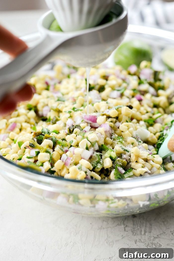 Chipotle's Signature Sweet Corn Salsa 9 Hands squeezing fresh lime juice over the partially mixed sweet corn salsa ingredients in a large bowl, emphasizing the addition of a key fresh and zesty component.