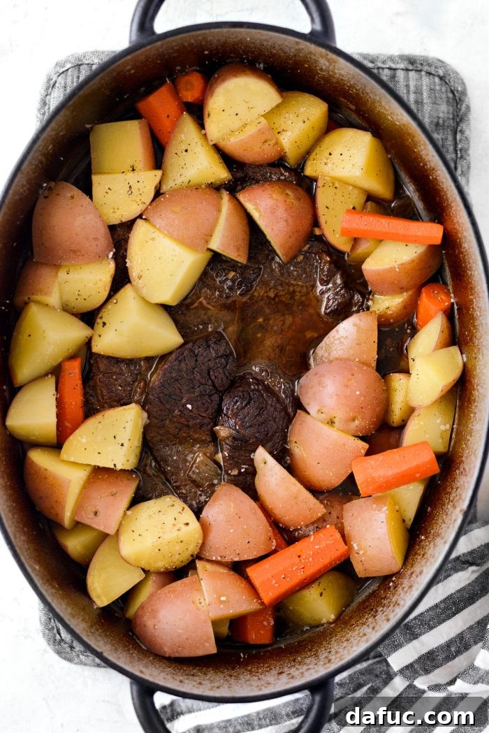 Hearty Homestyle Beef Pot Roast 15 Potatoes and carrots cooking with pot roast in a Dutch oven.