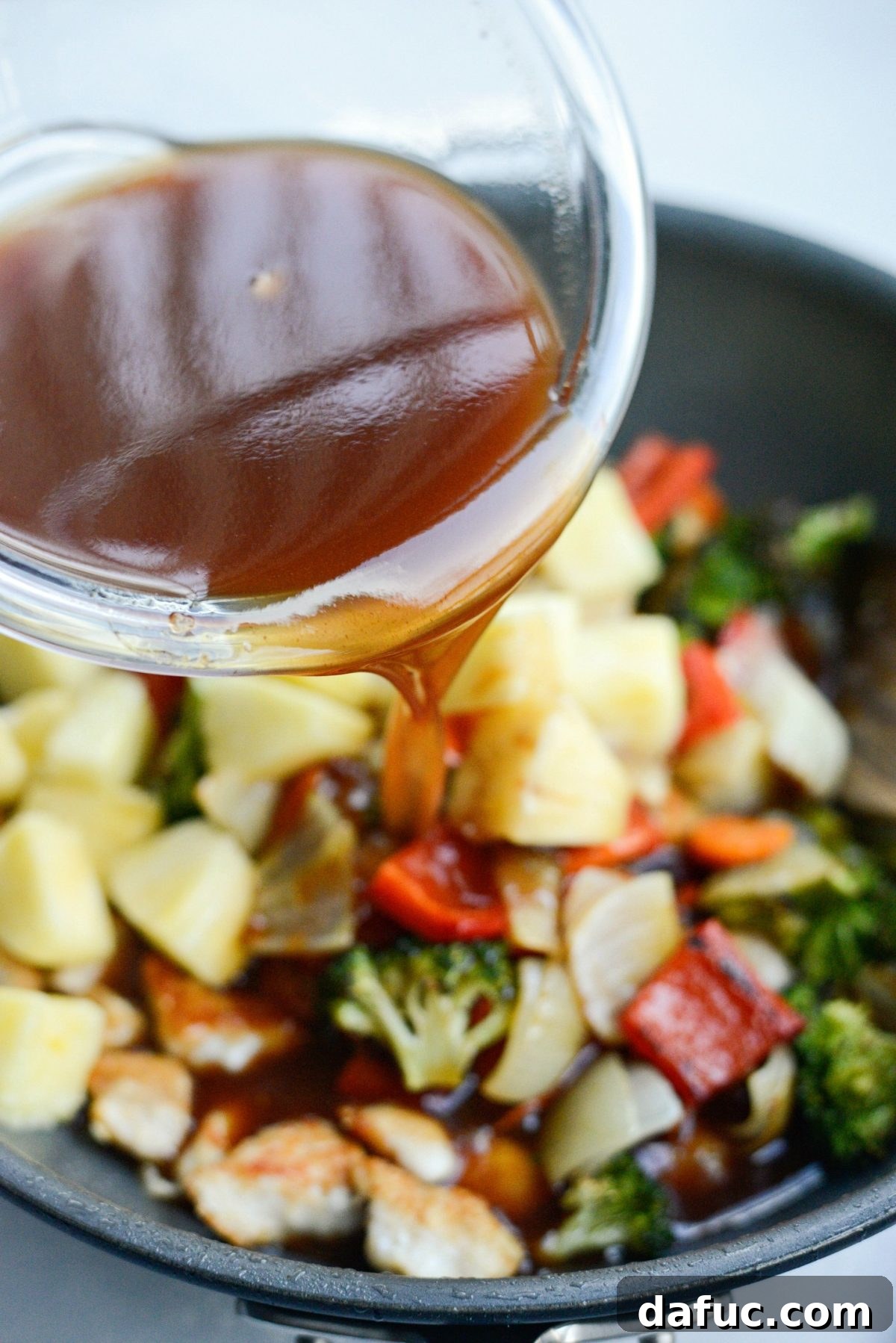Pouring sweet and sour sauce into the pan with chicken and vegetables.