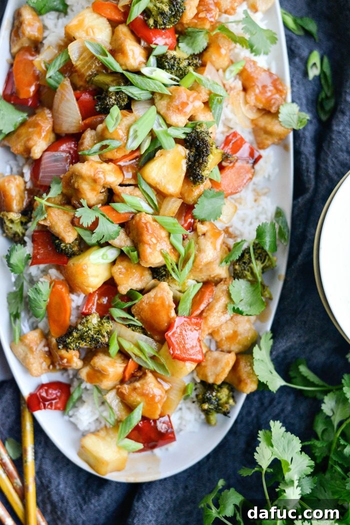 Homemade Sweet and Sour Chicken served on rice with sliced green onions and cilantro.