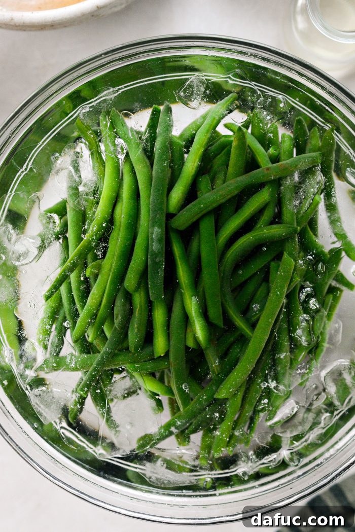 Crispy Shallot Green Bean Casserole 9 Blanched green beans being plunged into a bowl of ice water to stop the cooking process.