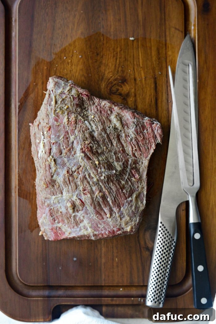 Succulent Corned Beef and Cabbage 13 Cooked corned beef brisket resting on a carving board, showing the direction of the grain for proper slicing