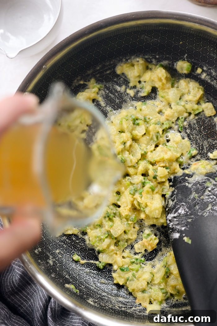 Pouring chicken broth and whole milk into the skillet while stirring the roux