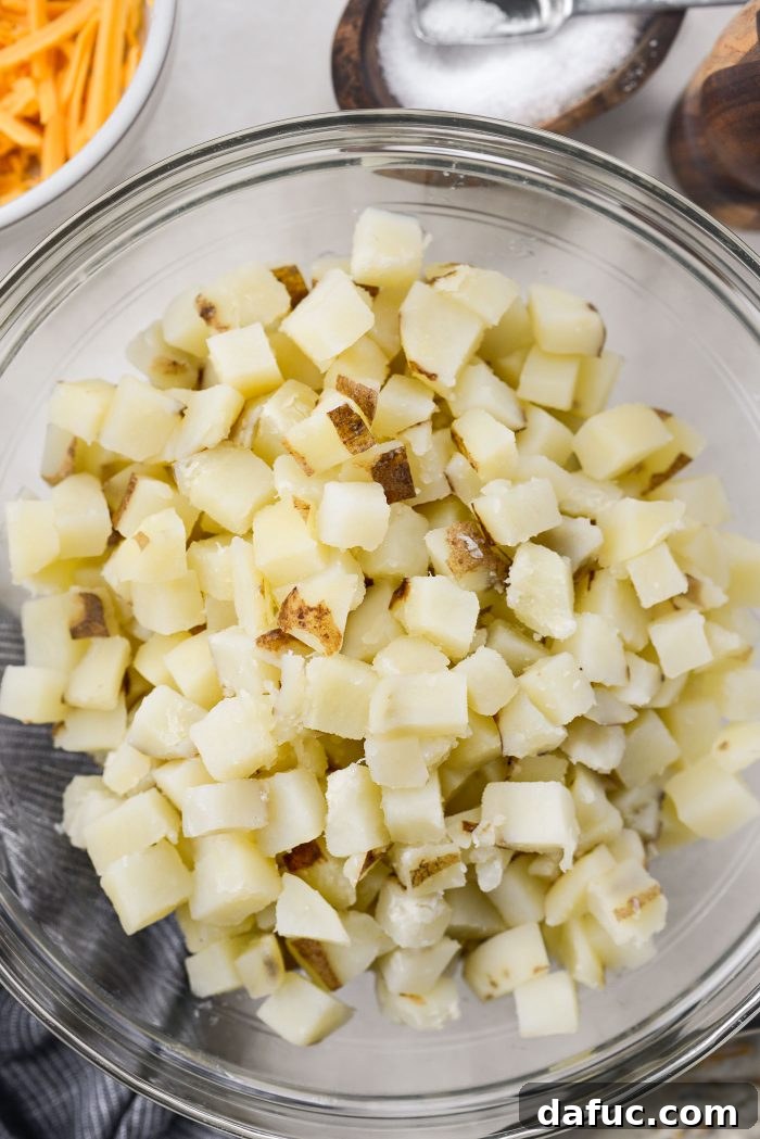 Cheesy potato mixture being transferred into a greased baking dish and topped with remaining cheddar