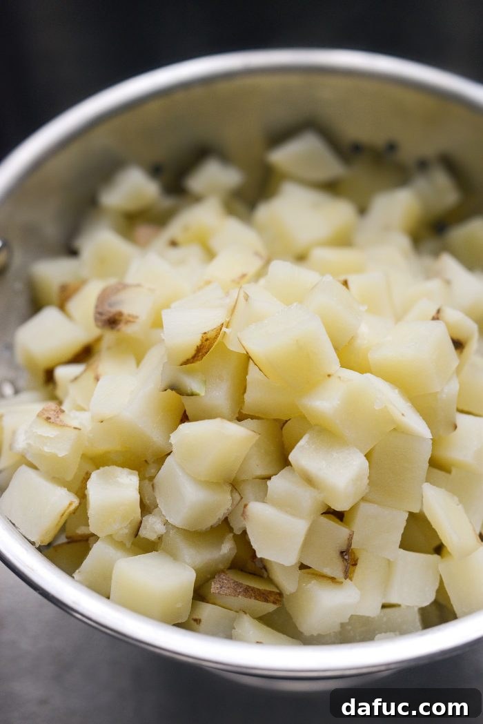 Partially cooked potatoes being drained in a colander in the sink