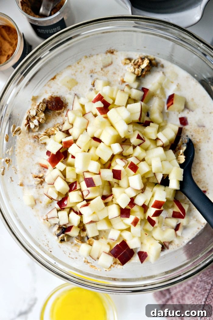 Warm Apple Cinnamon Oat Bake 7 Adding finely diced apples to the oatmeal mixture in a mixing bowl, ensuring even distribution of fruit