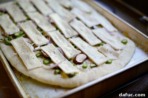Asparagus, mushrooms, shallots, and brie cheese arranged on a rolled-out flatbread dough, ready for baking.